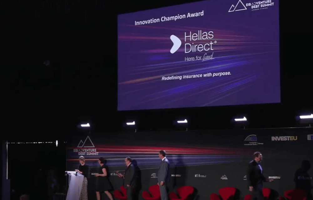 παρουσίαση σε προτζέκτορα, στην οθόνη το logo της Hellas Direct, άνθρωποι κάτω από τη σκηνή