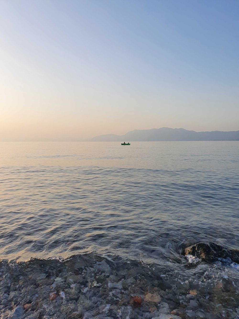 θάλασσα στο ηλιοβασίλεμα, μία βάρκα πλέει στα ήρεμα νερά