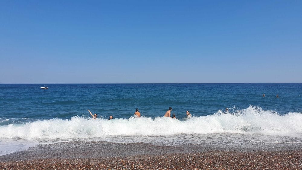 κύμα που σκάει στην παραλία, παρέα παιδιών παίζει μέσα στο νερό.