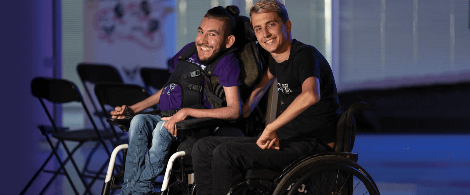 Δύο άντρες σε αναπηρικό αμαξίδιο, στο βάθος σπαστές μαύρες καρέκλες