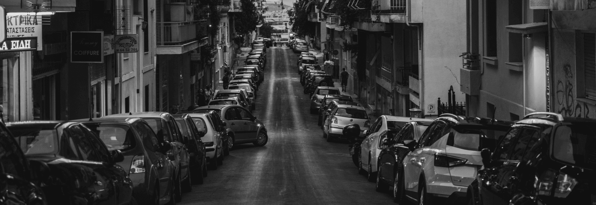 Ασπρόμαυρ εικόνα δρόμος στην πόληε με παρκαρισμένα αυτοκίνητα